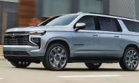 Grey 2026 Chevrolet Suburban driving through a city street with Chevrolet’s updated front-end styling.