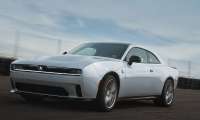 White 2026 Dodge Charger coupe driving on a racetrack in a front three-quarter action shot.