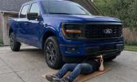 Ford F-150 owner lying beneath his truck with a flashlight to inspect rust on the underbody.
