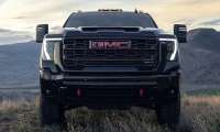 2026 GMC Sierra 2500 HD AT4 shown from the front on a grassy overlook with mountains in the background.