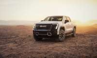 2026 GMC Sierra EV AT4 parked in a desert landscape at sunset with warm light behind it.