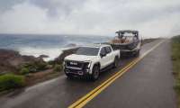 2026 GMC Sierra EV AT4 towing a boat along a coastal highway