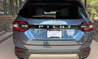 Rear view of a blue-gray 2026 Honda Pilot AWD parked under a covered driveway near a cabin.