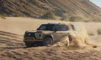 Lexus GX driving through deep sand with dust spraying around the SUV.