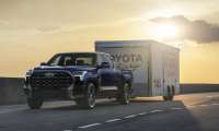 2026 Toyota Tundra Platinum towing an enclosed Toyota Racing trailer on the highway at sunset.