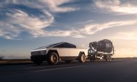 Tesla Cybertruck stainless steel electric pickup towing a large trailer on a highway at sunset