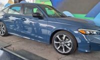 A dark blue 2025 Honda Civic is showcased indoors on a concrete surface. The car features modern design elements and curved lines, conveying a sense of elegance.