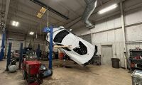 Chevrolet Corvette C8 lifted sideways on a vehicle lift inside an auto repair shop