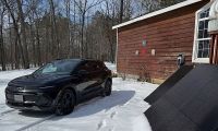 Chevrolet Equinox EV parked outside house connected to portable solar panels in snow