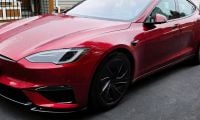 A red Tesla Model S Plaid shown from a front three-quarter angle, featuring its distinctive LED headlights and aggressive front design with black accents and wheels.