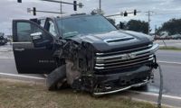 Black Chevrolet Silverado 3500 HD pickup truck with severe front-end collision damage, photographed at intersection with traffic lights overhead.