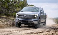 Silver Ford F-150 Lightning electric pickup truck driving off-road on rugged trail