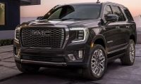 Black and silver 2025 GMC Yukon Denali parked in a desert landscape with rugged terrain and canyon cliffs.