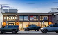 Rivian R1T and R1S electric vehicles parked outside a Rivian showroom at dusk.