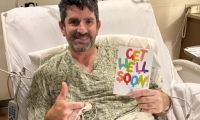 Jack's dad in a hospital bed smiles, holding a colorful "Get Well Soon" card. He gives a thumbs-up with his other hand. The mood is positive and hopeful.