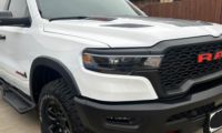White Ram 1500 pickup truck shown from a front three-quarter angle, featuring its distinctive black mesh grille with red Ram lettering and aggressive off-road bumper design.