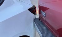 Close-up detail shot of a Ford F-150 truck's rear being dented in by a 2025 Tesla Model 3.