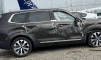 Jenni's black 2020 Kia Telluride with significant side damage and a deflated airbag visible in the driver's window, parked in a gravel lot near other vehicles and fencing.