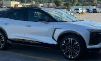 A white Chevrolet Blazer EV is shown from a front three-quarter angle in a parking lot, featuring distinctive black accents and two-tone alloy wheels.