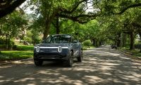 Rivian R1S electric SUV driving along a tree lined residential street in a suburban neighborhood