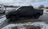 A black Ram 1500 pickup truck parked next to a metal railing in a snowy parking lot.