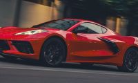 A red 2026 Corvette Stingray speeds down a city street at dusk. Motion blur highlights its aerodynamic design, reflecting a sense of power and excitement.