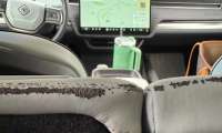 Close-up view of the rear seatback edge in Kate's 2023 Rivian R1S showing peeling upholstery material and surface degradation along a stitched section of the light-colored seat trim.