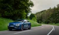 Blue Audi Q4 e-tron electric SUV driving on a winding forest highway in motion