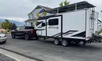 Black GMC Sierra pickup towing an Imagine XLS travel trailer on a suburban street near houses.