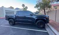 Black Toyota Tacoma shown in side profile parked in a residential parking lot.