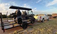 White Chevrolet Silverado towing a golf cart trailer on the roadside with a tow truck parked ahead.
