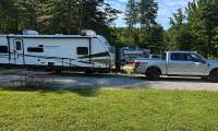 Ford F-150 pickup towing an Astoria travel trailer at a green campground site.
