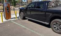 Black Ford F-150 Lightning charging at a ChargePoint station in a sunny parking lot.