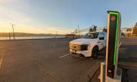 White Ford F-150 Lightning charging at a Rivian station near the waterfront at sunset.