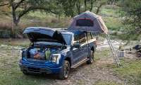 Blue Ford F-150 Lightning XLT set up at a campsite with an open frunk and rooftop tent.