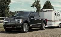 Black Ford F-150 Platinum towing a horse trailer at a ranch, with a person leading a horse alongside a wooden fence