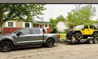 Ford F-150 pickup shown towing a yellow Jeep Wrangler on a flatbed trailer