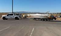 White Ford F-150 pickup towing a flame-graphic speedboat on a triple-axle trailer in a desert parking lot