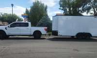 White Ford F-150 towing a large enclosed cargo trailer in a full side view on a residential street.