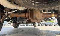 Close-up under a Ford F-150 XLT showing rust on the rear axle and differential while parked on a dealer lot.