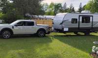 White Ford Maverick towing an Avenger LT camper trailer in a grassy yard.