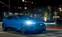 Blue Ford Mustang Mach-E electric SUV driving at night on a city street with headlights on.