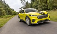 Yellow Ford Mustang Mach-E Rally electric SUV kicking up dust while driving on a gravel dirt road