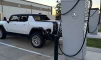 White GMC Hummer EV pickup charging at a Mercedes-Benz charging station at sunset.