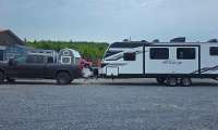 GMC Sierra AT4 HD towing an Imagine travel trailer in a side-profile view on a gravel lot.