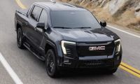 Black GMC Sierra EV electric pickup driving on a winding mountain highway, showcasing performance, LED lighting, and rugged design.