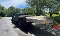 Black GMC Sierra EV towing a canoe on a small trailer in a residential driveway.