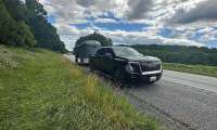 Black GMC Sierra EV parked on the roadside while towing a horse trailer under a cloudy sky.