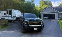 Black GMC Sierra EV parked in a driveway while towing a Winnebago Micro Minnie camper trailer.