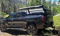Gregg’s GMC Sierra EV Denali parked at a wooded campsite with overlanding gear mounted in the bed.